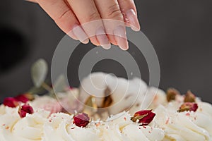 The condater sprinkles the cake with grated almonds and coconut. Close-up of a hand and pouring crumbs.