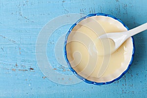 Condensed milk or evaporated milk in bowl on blue table top view.