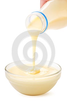 Condensed milk from the package is poured into a plate on a white background. Isolated