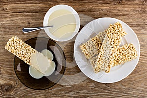 Condensed milk poured on puffed rice in saucer, bowl with condensed milk, puffed rice in plate on table. Top view