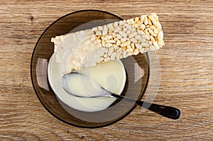 Condensed milk poured on puffed rice, spoon in brown saucer on wooden table. Top view
