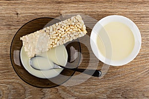 Condensed milk poured on puffed rice, spoon in saucer, bowl with milk on table. Top view