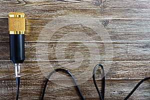 Condenser gold microphone with cable lies on a wooden table with copy space. Musical theme. Flat lay.