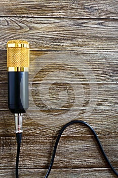Condenser gold microphone with cable lies on a wooden table with copy space. Musical theme. Flat lay.