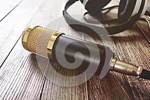 Condenser gold microphone and headphones lies on a wooden table. The light from left side.