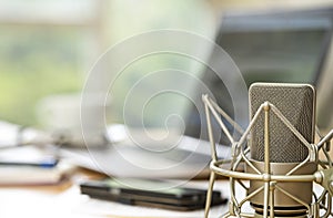 Condenser microphone close up in front of a blurred workspace wi