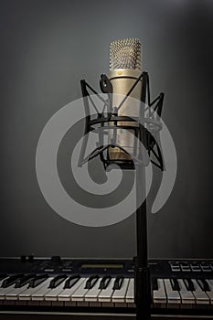 A condenser microphone in a home studio in front of a keyboard.