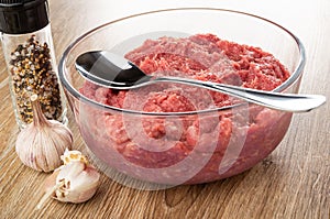 Condiment in jar, garlic, spoon in bowl with raw chicken forcemeat on table