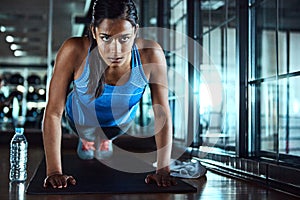 Conditioning her body. an attractive young woman doing pushups as part of her workout in the gym.