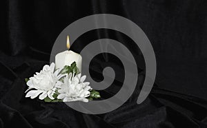 Condolence card. White burning candle and white flowers on a black background, free space for text