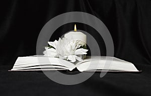 Condolence card. A white memorial candle with white flowers and an open book. The funeral, the sadness.