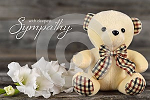 Condolences card with teddy bear and white flower on wooden background
