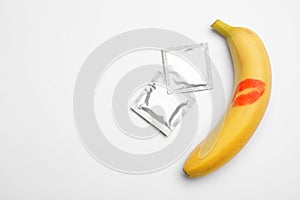 Condoms and banana with  kiss mark on white background, top view. Safe sex