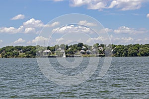 Condos beside the lake among the trees under a cloudy blule sky with a sailboat and a pontoon out on the water