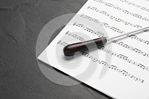 Conductor`s baton and sheet music on black background, closeup view photo