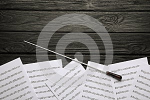 Conductor`s baton and sheet music on black wooden table, flat lay. Space for text photo