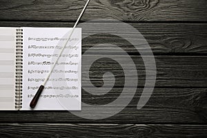 Conductor`s baton and sheet music book on black wooden table, top view. Space for text photo