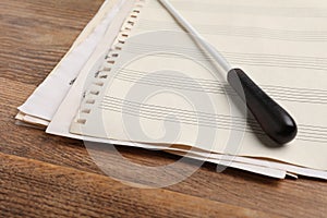 Conductor`s baton and sheet music on wooden table, closeup photo
