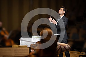 Conductor of symphony orchestra with performers in background in concert hall