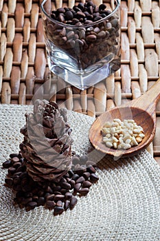 Cone, pine nuts in the glass and shelled nuts in the wooden spon on the braided surface. photo