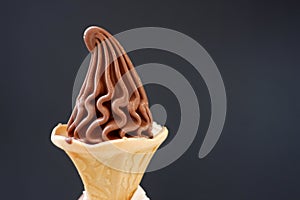 A cone of soft chocolate ice cream on dark background with copy space