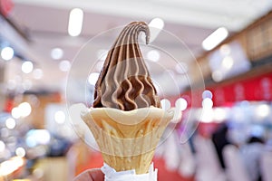 A cone of soft chocolate ice cream on  female hand with blurred inside a aisle of department store