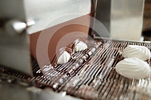 Confectionary conveyor is covering marshmallow with liquid chocolate.