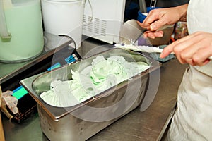 Confectioner in chef uniform is working at ice cream factory. Woman is decorations of italian creamy mint ice cream flavors.