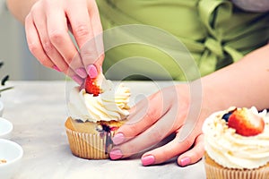 Confectioner decorate cupcakes with cream cheese and fruits, close up. Cakes, confectionery. Desserts. Professional confectioner