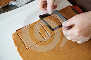 The confectioner forms gingerbread cookies using an original rectangular cutting. Woman& x27;s hands in protective gloves