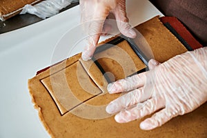 The confectioner forms gingerbread cookies using an original rectangular cutting. Woman& x27;s hands in protective gloves