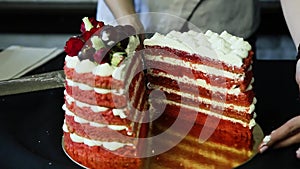 Confectioner hands cut down red decorated cake into two parts