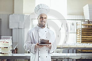 Confectioner man holding cake smiling in a pastry shop