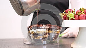 Confectioner pouring hot chocolate over layered dessert in transparent form