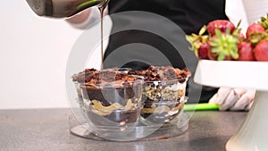 Confectioner pouring hot chocolate over layered dessert in transparent form.