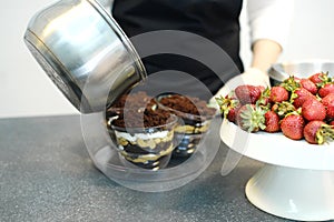 Confectioner pouring hot chocolate over layered dessert in transparent form