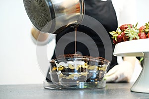 Confectioner pouring hot chocolate over layered dessert in transparent form