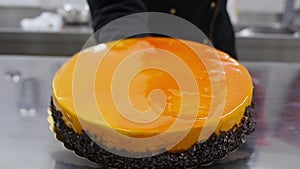 A confectioner puts a fresh made orange cake on a table