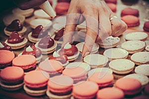 Confectioner's hands filling macarons with pink ganache cream