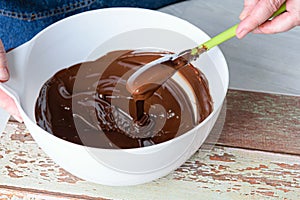 Confectioner tempering chocolate with a spatula in a white bowl photo