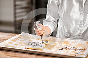 Confectioners hand squeezing pastry bag over eclair