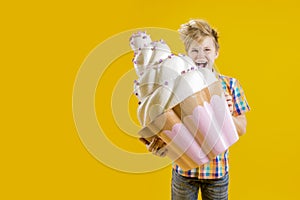 Confectionery. A cute boy holding a huge cupcake in his hands, trying to bite him on a yellow background. Delicious dessert.