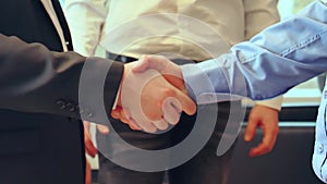 In conference hall, three men in business attire engage in firm handshake to seal a deal. The handshake symbolises trust