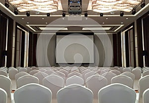 Conference Meeting Room with ceiling LED lights, Row of White Chairs, with Stage and Empty Screen for Business Meeting, Conference