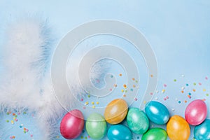 Confetti, bunny ears and colorful Easter eggs on blue table top view. Funny Easter greeting card. Copy space for text.