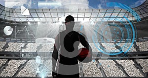 Confetti falling over silhouette of male basketball player holding basketball against sports stadium