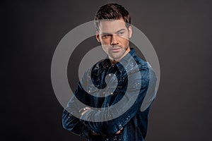 Confidence and charisma. Good looking young man keeping arms crossed and looking away while standing against grey background