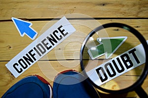 Confidence or Doubt opposite direction signs in magnifying with sneakers and eyeglasses on wooden