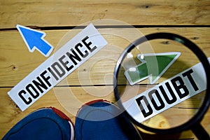 Confidence or Doubt opposite direction signs in magnifying with sneakers and eyeglasses on wooden photo