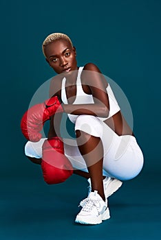 Confidence radiates off of her. Full length portrait of an attractive young female boxer crouching against a dark